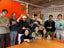 Group of people holding plants in an indoor setting with orange walls and a wooden table.